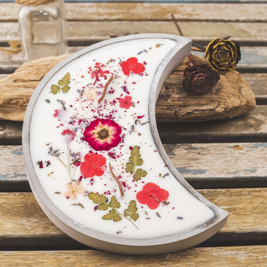 La Vela Aromática Fleur-de-Bois en Cuenco de Cemento en Forma de LUNA con Mecha Ondulada, adornada con flores secas y hojas, descansa sobre madera rústica-el detalle perfecto para un regalo especial.