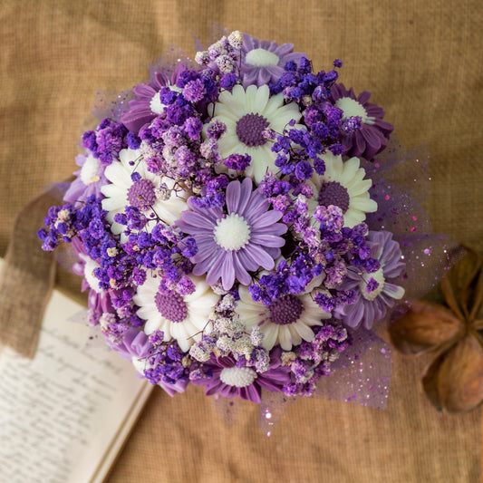 El Ramo de Flores Margaritas Clásico de Cera de Soja FRESCURA DE LAVANDA de Fleur-de-Bois, con margaritas blancas y moradas y pequeñas flores moradas, descansa sobre arpillera junto a un cuaderno abierto, constituyendo un encantador regalo romántico.