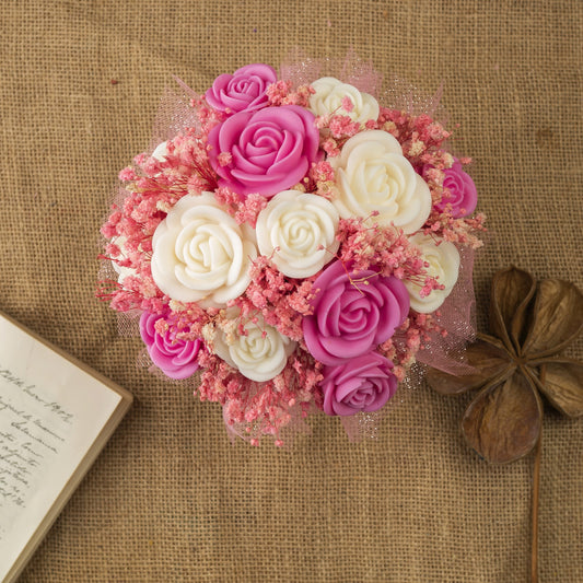 El Ramo de Rosas Clásico de Cera de Soja PERLA DE POMA de Fleur-de-Bois, en tonos rosa y blanco con paniculata, presentado sobre arpillera junto a un diario abierto y una vaina seca, es el regalo romántico ideal.