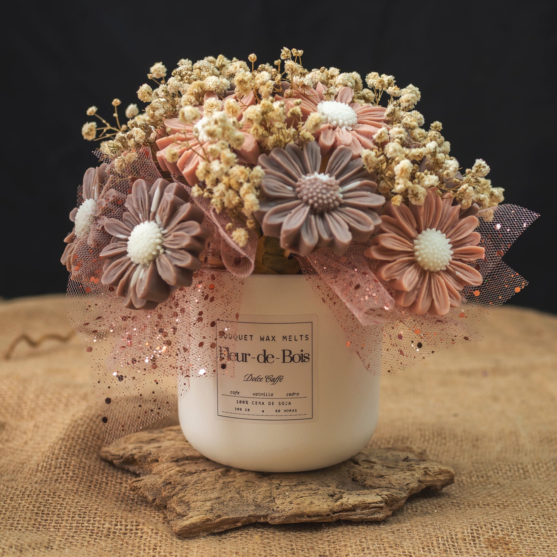 Un tarro blanco con la etiqueta Fleur-de-Bois contiene el Ramo de Flores Margaritas Clásico de Cera de Soja DOLCE CAFFÉ, adornado con tul rosa, purpurina y aliento de bebé seco para un regalo romántico, sobre un fondo oscuro.