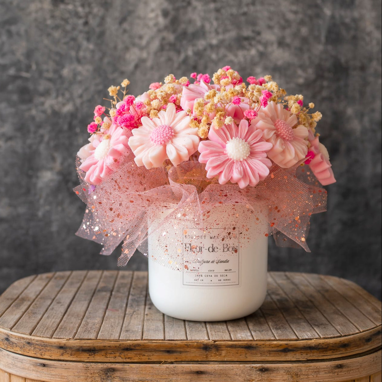 El Ramo de Flores Fleur-de-Bois Margaritas Clásico de Cera de Soja DULZURA DE SANDÍA presenta flores artificiales rosas y blancas con cinta y acentos secos, dispuestas cerca de velas derretidas sobre madera para una exhibición romántica.