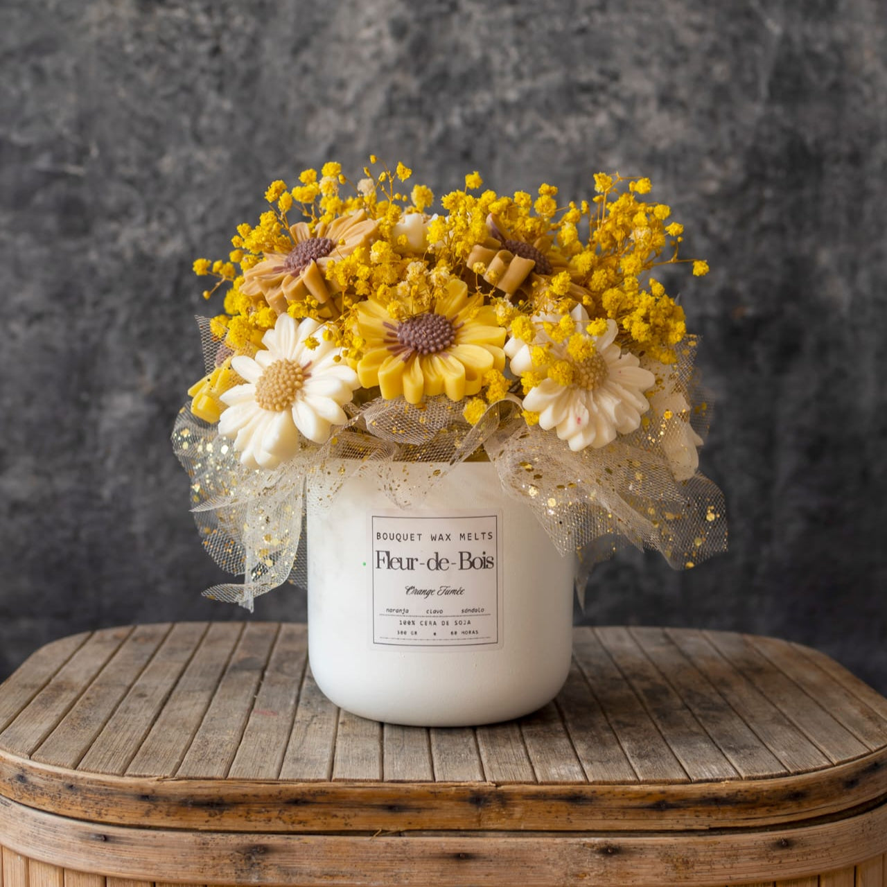 El tarro Fleur-de-Bois contiene el Ramo de Flores Margaritas Clásico de Cera de Soja ORANGE FUMÉE, arreglado con malla decorativa y colocado sobre madera sobre un fondo gris: un regalo romántico ideal.