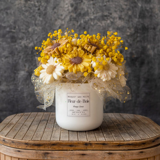 El tarro Fleur-de-Bois contiene el Ramo de Flores Margaritas Clásico de Cera de Soja ORANGE FUMÉE, arreglado con malla decorativa y colocado sobre madera sobre un fondo gris: un regalo romántico ideal.