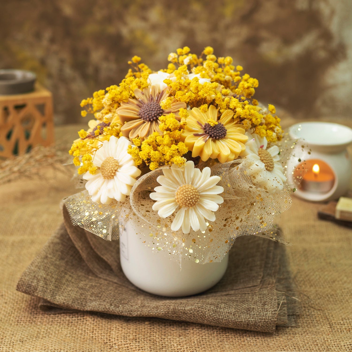 El Ramo de Flores Margaritas Clásico de Cera de Soja Fleur-de-Bois ORANGE FUMÉE de Fleur-de-Bois presenta margaritas amarillas y blancas en una maceta de cerámica, colocadas sobre arpillera con una vela: un regalo romántico ideal con encanto rústico.