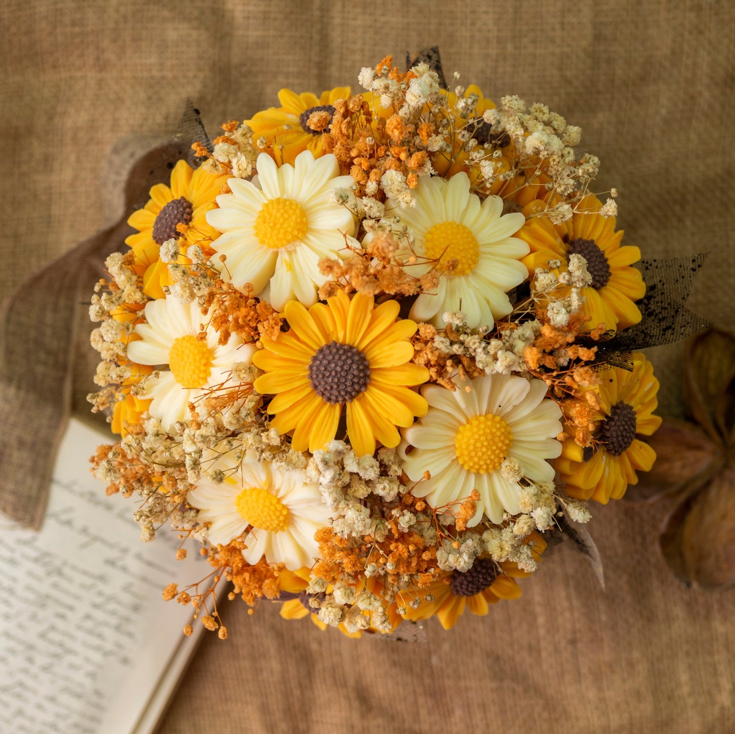 El Ramo de Flores Margaritas Clásico de Cera de Soja Fleur-de-Bois PEAKY SPOOKY de Fleur-de-Bois presenta flores amarillas y blancas como margaritas y velas derretidas florales-un perfecto regalo romántico expuesto sobre tela marrón rústica.