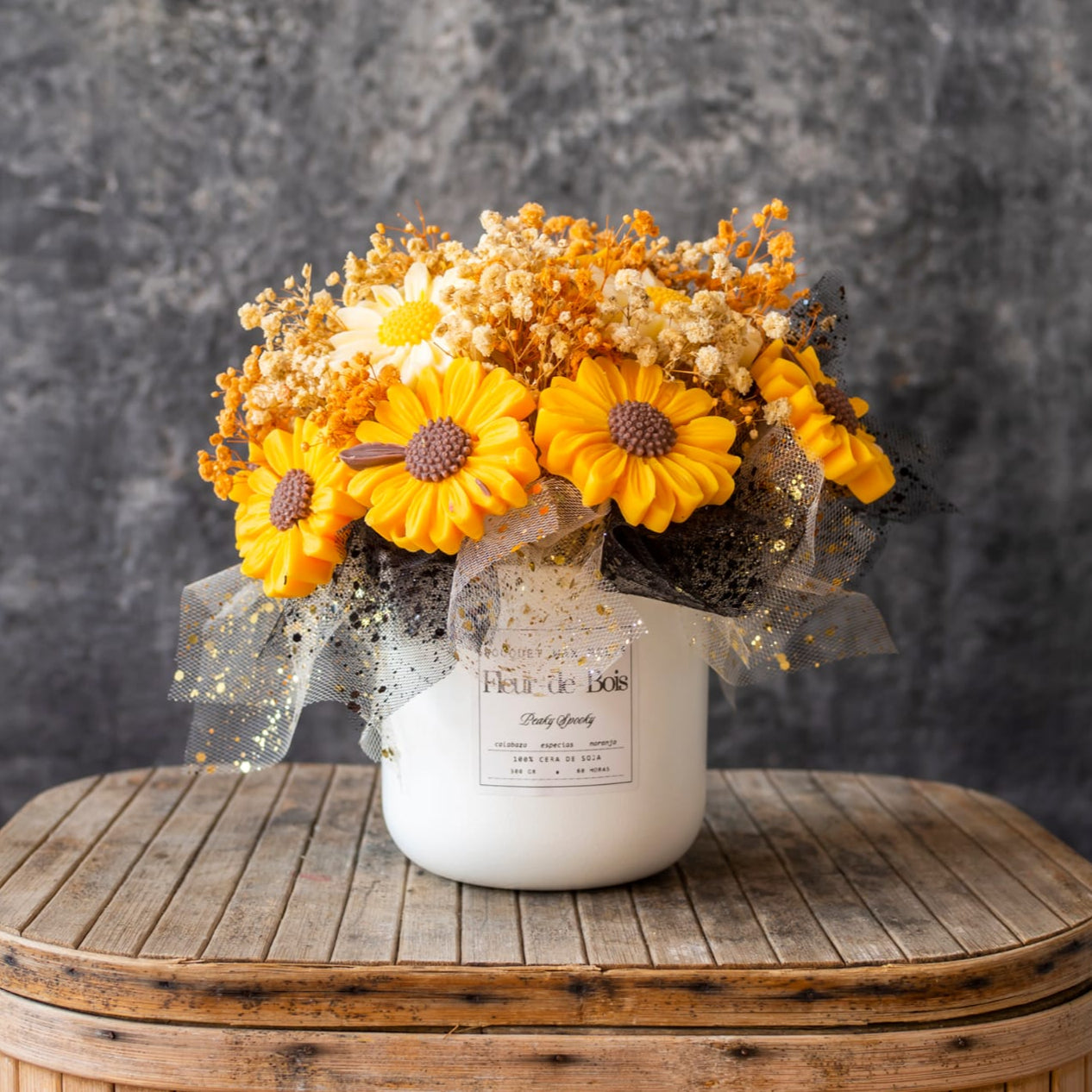 Un jarrón blanco con etiqueta exhibe las Margaritas Ramo de Flores Clásico de Cera de Soja PEAKY SPOOKY de Fleur-de-Bois -flores secas blancas y naranjas con una cinta de puntos- sobre una mesa de madera rústica, perfectas como regalo romántico.