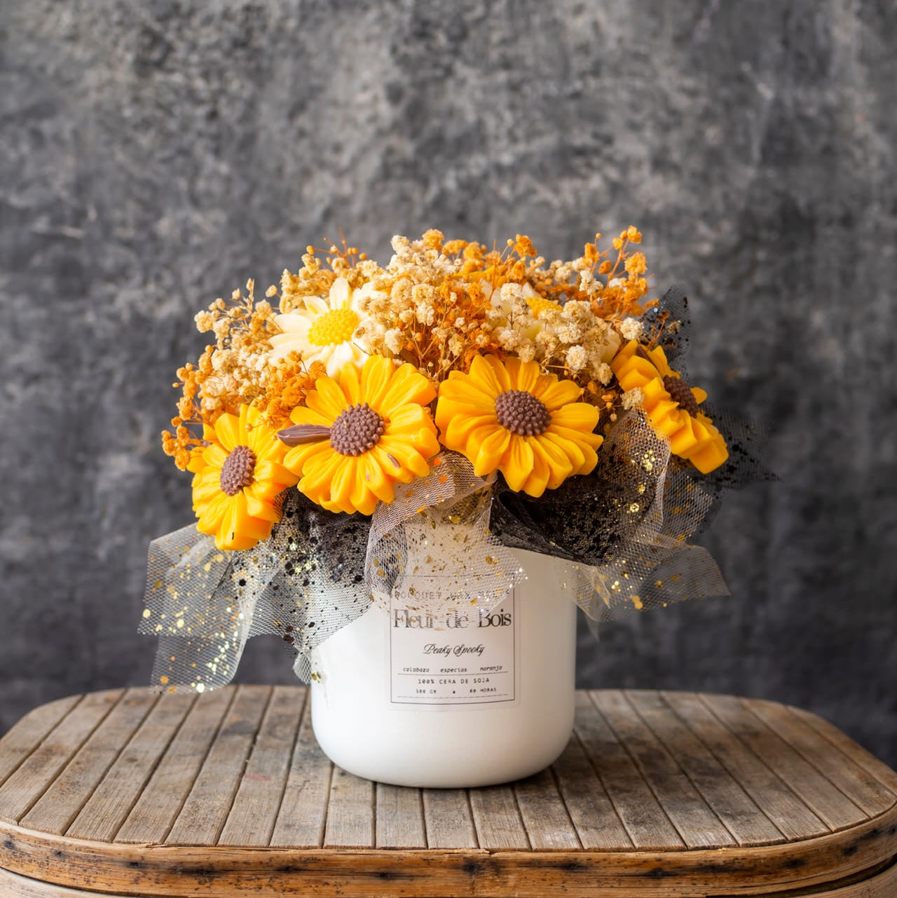 Un jarrón blanco con etiqueta exhibe las Margaritas Ramo de Flores Clásico de Cera de Soja PEAKY SPOOKY de Fleur-de-Bois - flores en cera de soja y secas blancas y naranjas con una cinta de puntos - sobre una mesa de madera rústica, perfectas como regalo romántico.