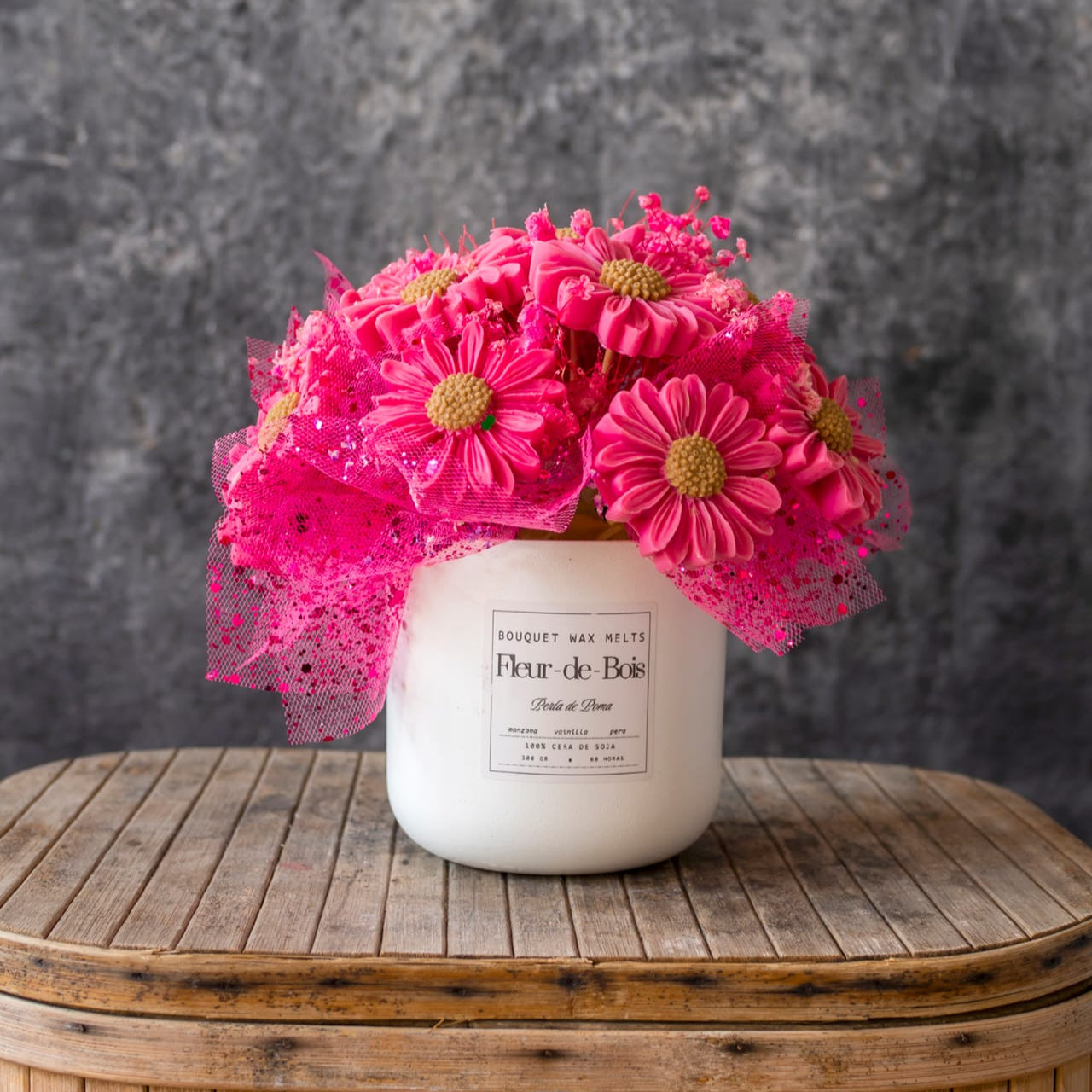Un tarro blanco de Flor de Bois con la etiqueta PERLA DE POMA contiene un Ramo de Flores Margaritas Clásico de Cera de Soja, con flores de cera rosa y malla sobre madera: el regalo romántico perfecto.