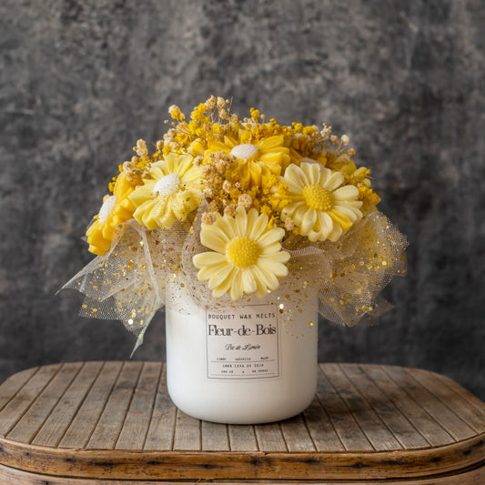El Ramo de Flores Fleur-de-Bois Margaritas de Cera de Soja PIE DE LIMÓN, con margaritas amarillas y blancas en un jarrón blanco con tul de puntos dorados, es un regalo romántico ideal sobre un fondo gris texturizado.
