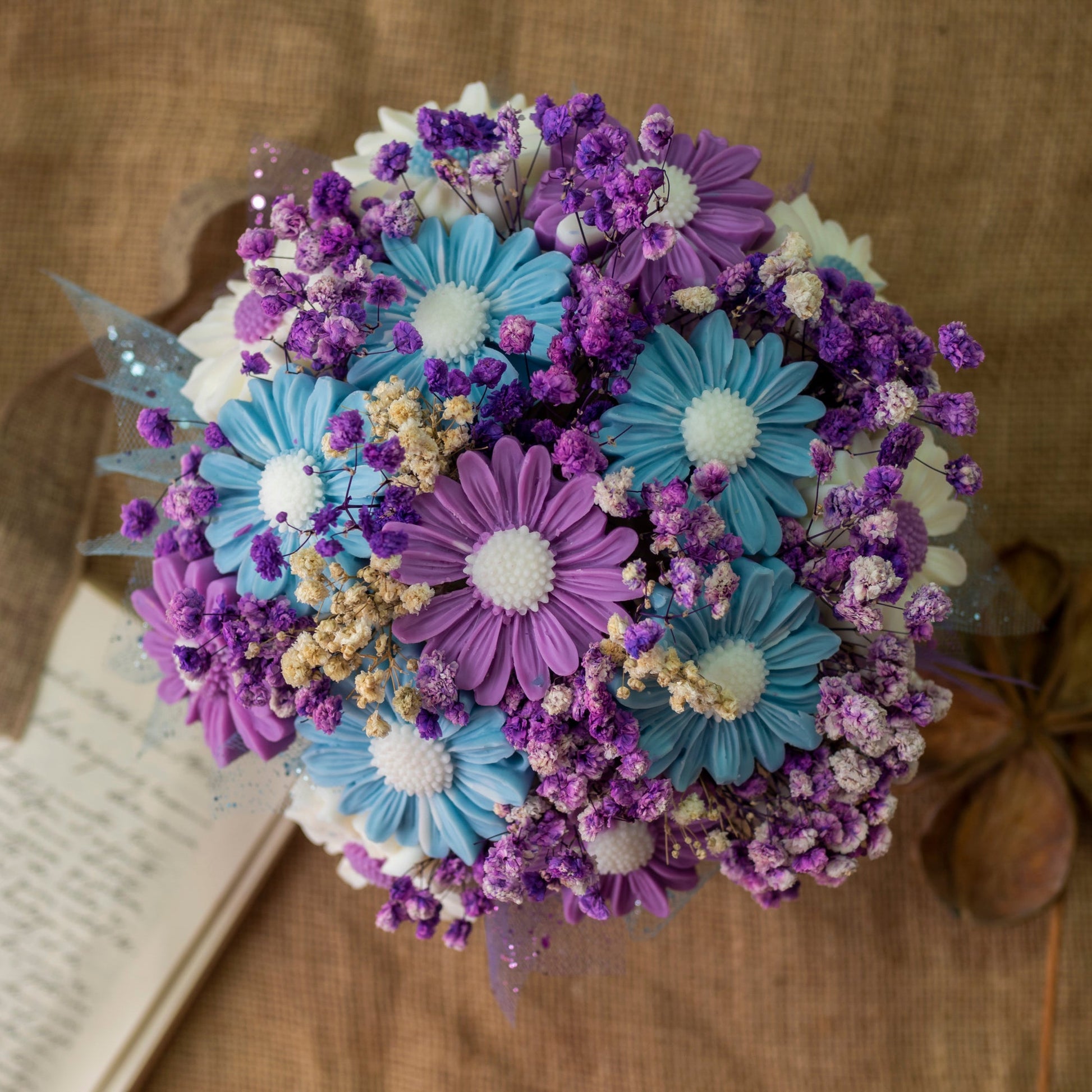El Ramo de Flores Margaritas Clásico de Cera de Soja Fleur-de-Bois MADERA MORADA de Fleur-de-Bois, con margaritas azules y moradas con flores blancas, es un regalo romántico perfecto bellamente arreglado sobre arpillera.