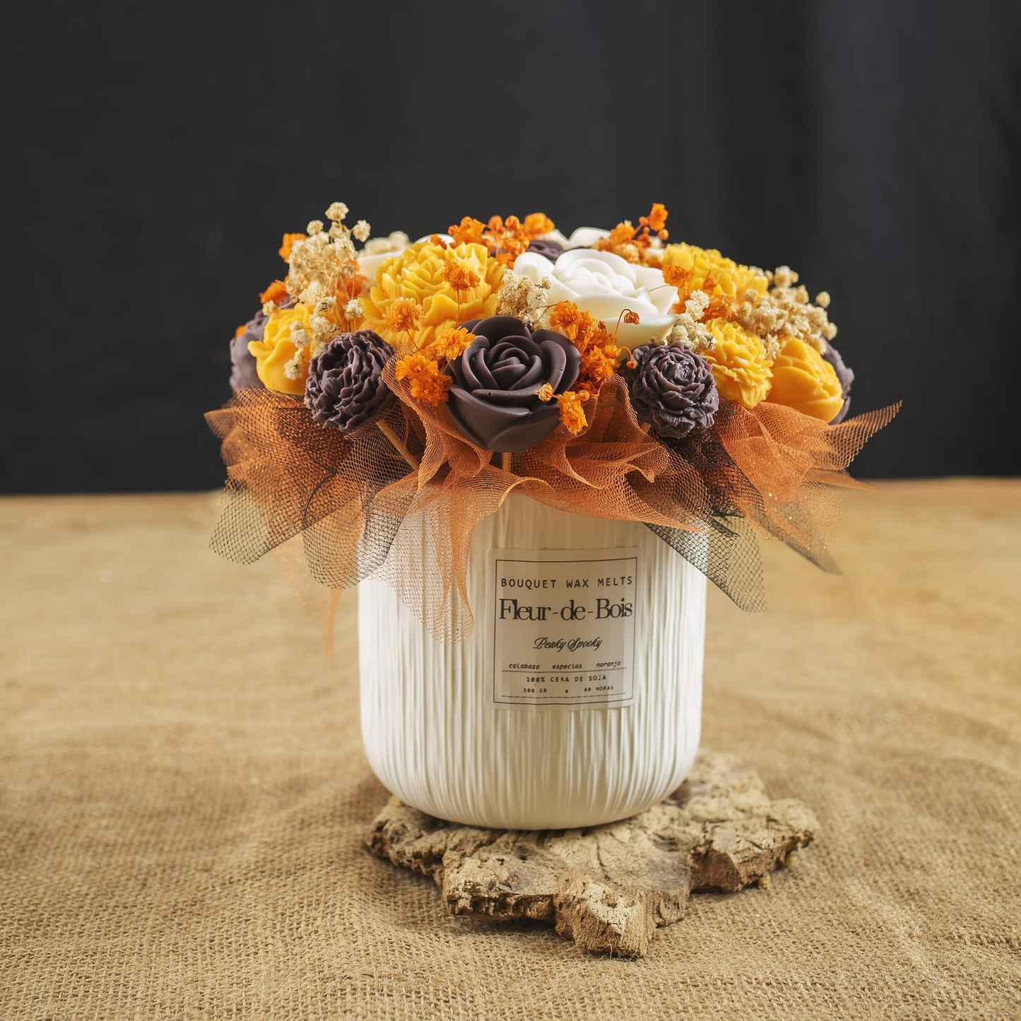 El arreglo «Ramo de peonías y rosas clásico de cera de soja PEAKY SPOOKY» de Fleur-de-Bois presenta unas vibrantes peonías y rosas artificiales en un jarrón de cerámica blanca con tul, sobre una base de madera rústica y arpillera: un regalo original que destaca sobre un fondo negro.
