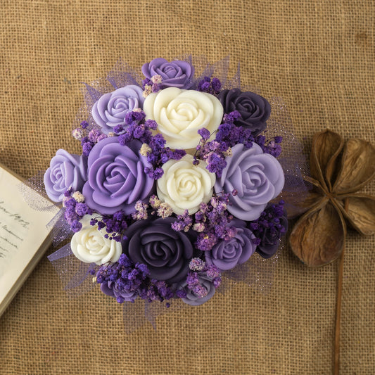 El Ramo de Rosas Clásico de Cera de Soja FRESCURA DE LAVANDA de Fleur-de-Bois, con velas de soja en forma de flor morada, lavanda y blanca, descansa sobre arpillera junto a un libro abierto y una flor seca, ideal para un regalo romántico.
