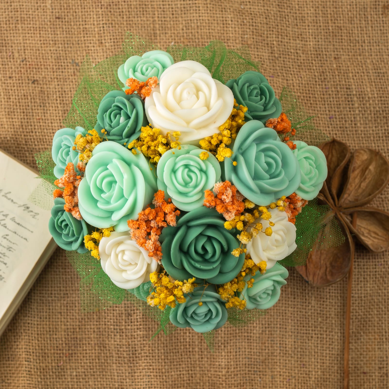 El Ramo de Rosas Clásico de Cera de Soja Fleur-de-Bois LIMA SAUVAGE de Fleur-de-Bois tiene rosas verde azulado, blancas y verdes con relleno amarillo anaranjado sobre arpillera. Incluye velas derretidas en forma de flor y vainas secas, ideal como regalo romántico.