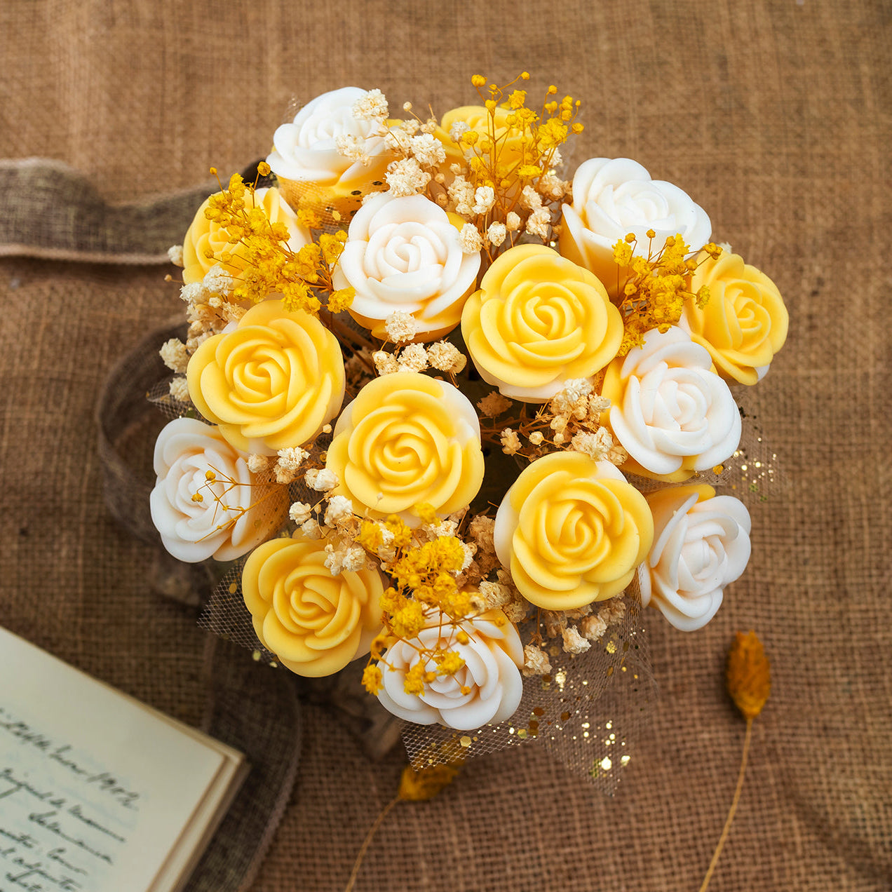 El Ramo de Flores Rosas CLÁSICO PIE DE LIMÓN de Fleur-de-Bois, hecho con cera de soja en tonos amarillo y blanco, sobre arpillera y junto a un cuaderno abierto. Un regalo romántico ideal para sorprender a alguien especial.