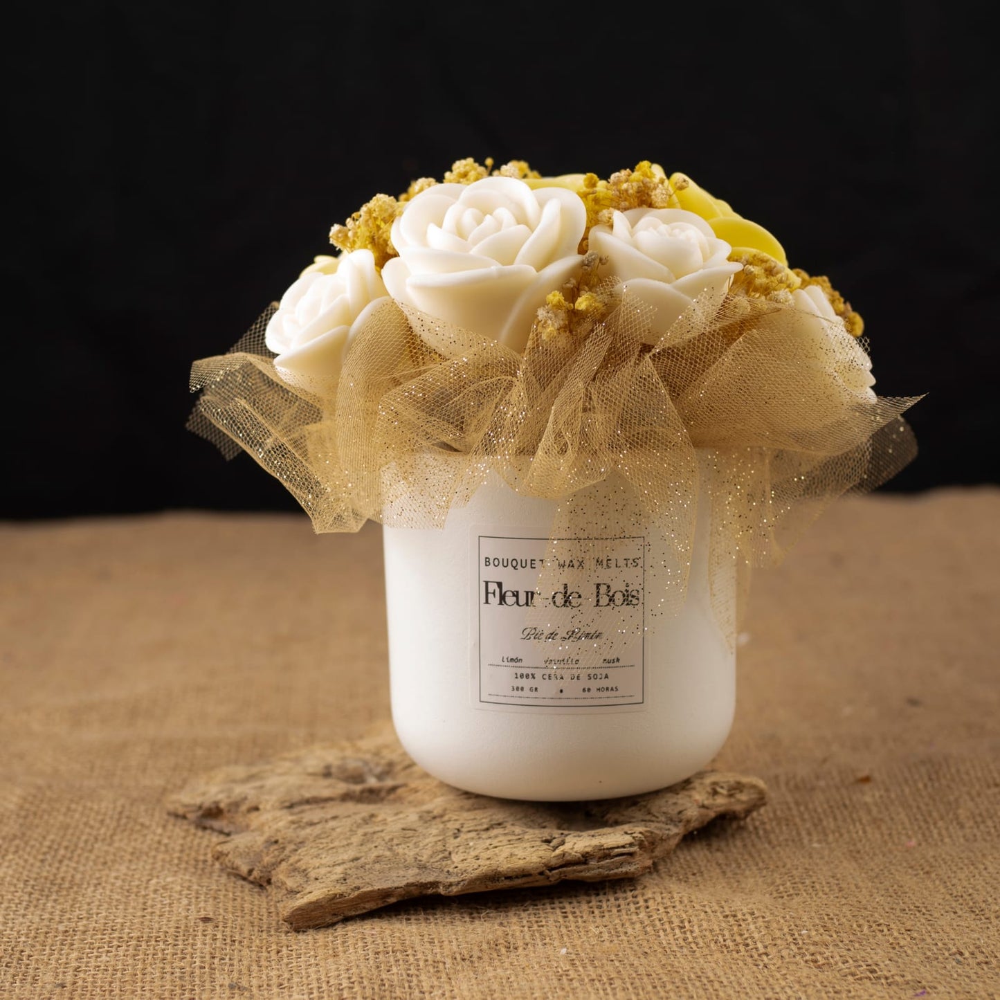 Un tarro blanco de Flor de Bois contiene el Ramo de Rosas Clásico de Cera de Soja PIE DE LIMÓN -rosas blancas artificiales y flores amarillas con tul dorado- colocado sobre madera con fondo de arpillera y negro, ideal como regalo romántico.