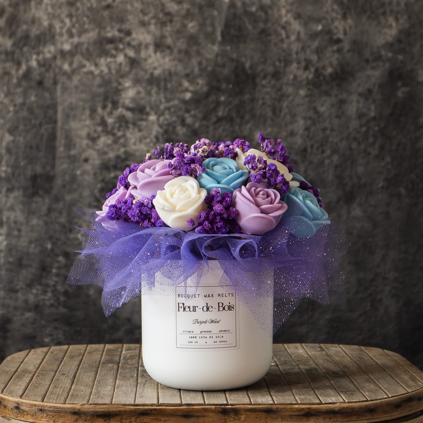 El Ramo de Rosas Clásico de Cera de Soja PURPLE WOOD de Fleur-de-Bois presenta rosas moradas, azules y blancas con aliento de bebé en un jarrón blanco -un regalo romántico ideal- expuestas sobre madera rústica contra un fondo gris texturizado.