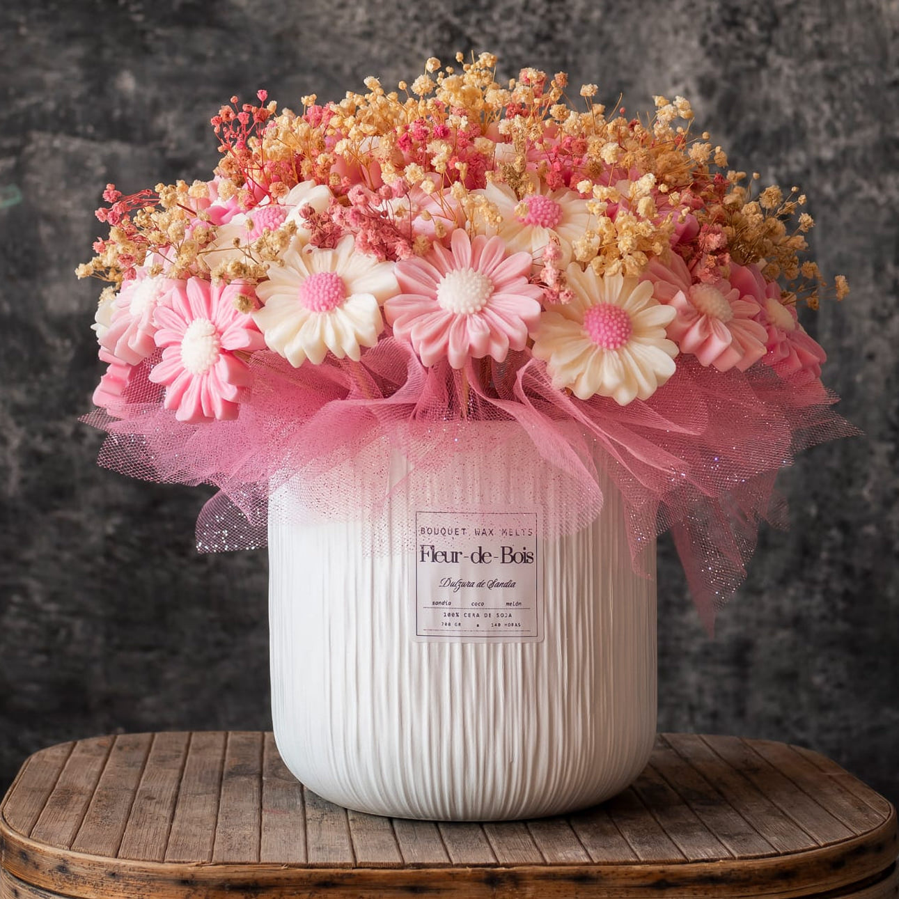 Un jarrón blanco con textura contiene el Ramo de Margaritas GRANDE de Cera de Soja de Fleur-de-Bois -flores de cera de soja rosas y blancas con aliento de bebé seco y tul rosa- expuestas sobre madera sobre un fondo de textura oscura.