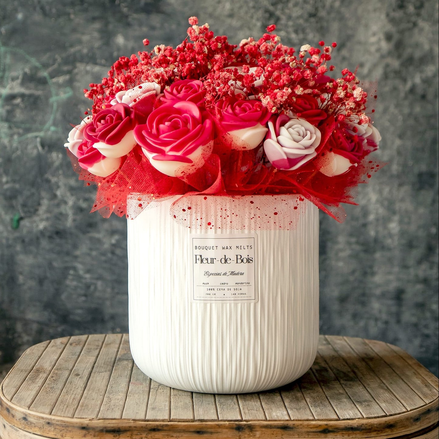 El Ramo de Rosas GRANDE de Cera de Soja de Fleur-de-Bois, acentuado con aliento de bebé rojo y malla en un jarrón de textura blanca, crea el regalo romántico perfecto en una mesa rústica sobre un fondo oscuro.