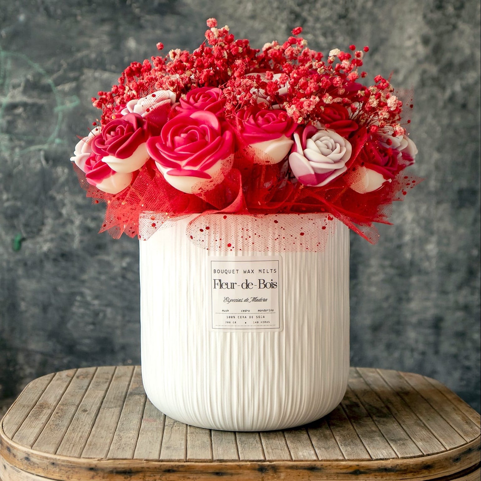 El Ramo de Rosas GRANDE de Cera de Soja de Fleur-de-Bois, acentuado con aliento de bebé rojo y malla en un jarrón de textura blanca, crea el regalo romántico perfecto en una mesa rústica sobre un fondo oscuro.