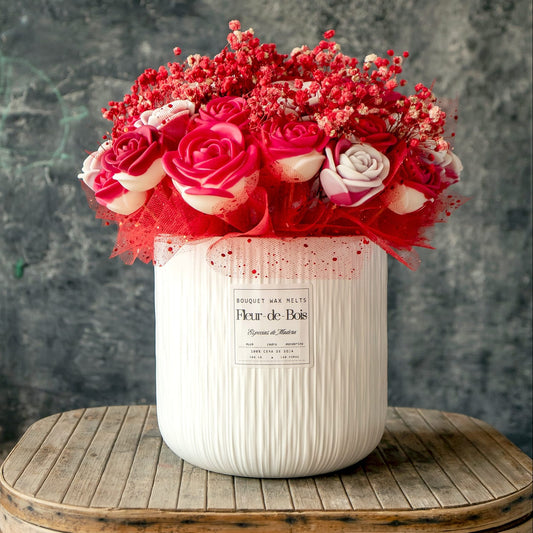 El Ramo de Rosas GRANDE de Cera de Soja de Fleur-de-Bois, acentuado con aliento de bebé rojo y malla en un jarrón de textura blanca, crea el regalo romántico perfecto en una mesa rústica sobre un fondo oscuro.