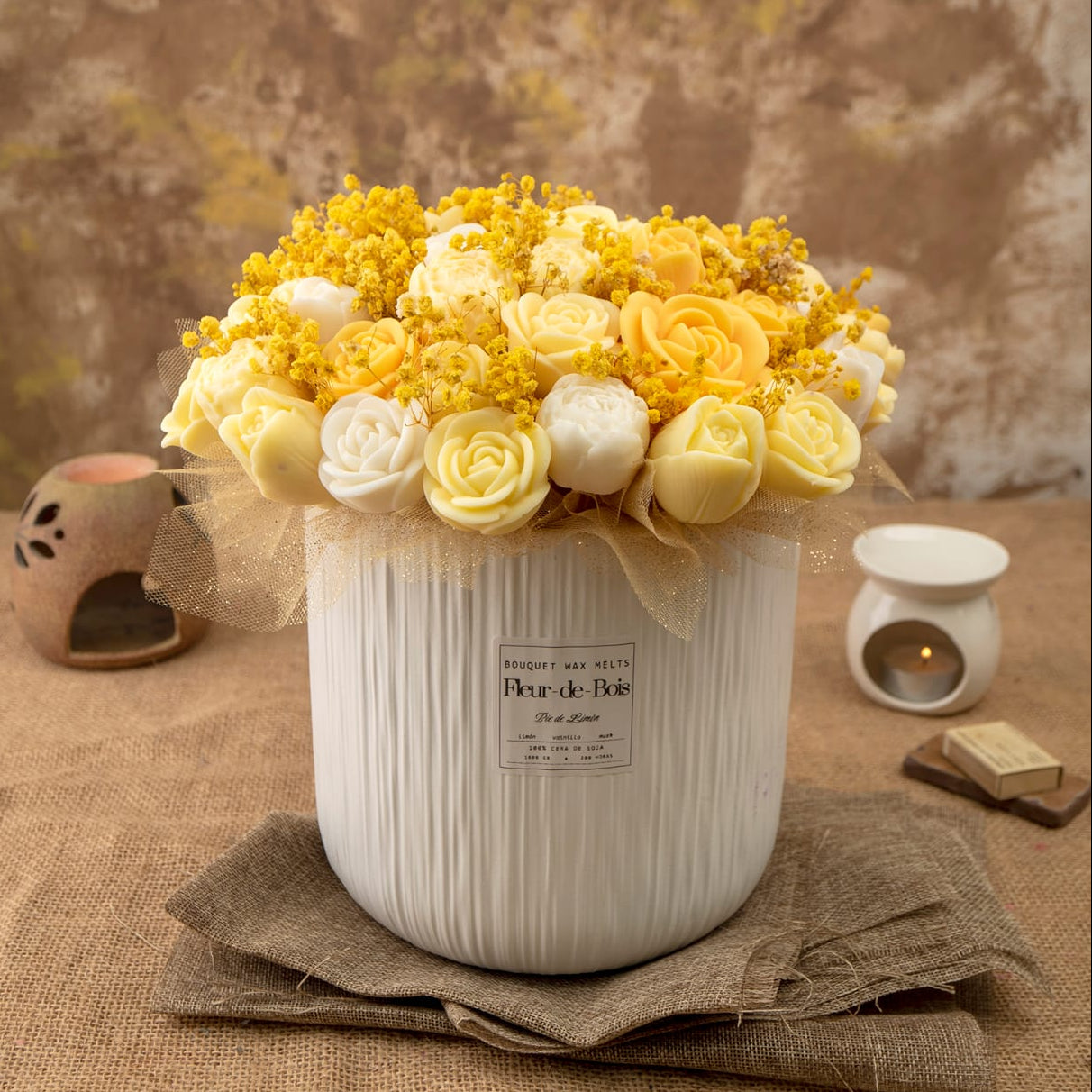 El Ramo de Rosas, Tulipanes y Peonias XL de Cera de Soja de Fleur-de-Bois, con flores blancas y amarillas en un jarrón blanco sobre arpillera, vela floral y libro al fondo-el regalo romántico ideal.