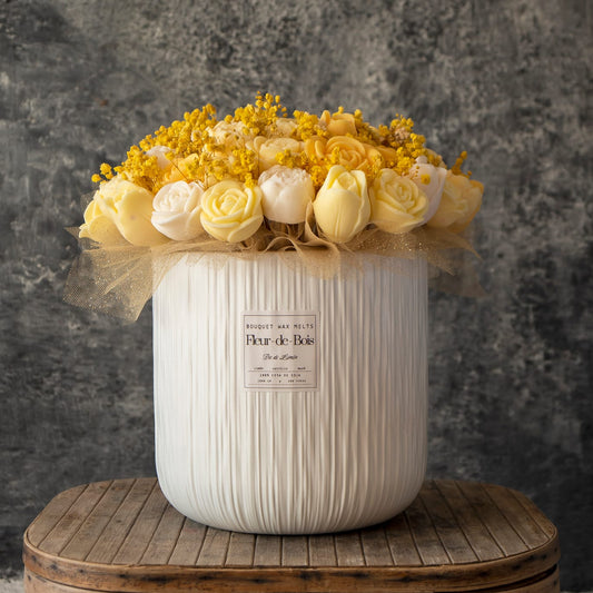 Un jarrón de textura blanca con el XL Ramo de Rosas, Tulipanes y Peonias de Cera de Soja de Fleur-de-Bois, adornado con tul dorado, descansa sobre madera ante un fondo gris-un perfecto regalo romántico con el sello Fleur-de-Bois.