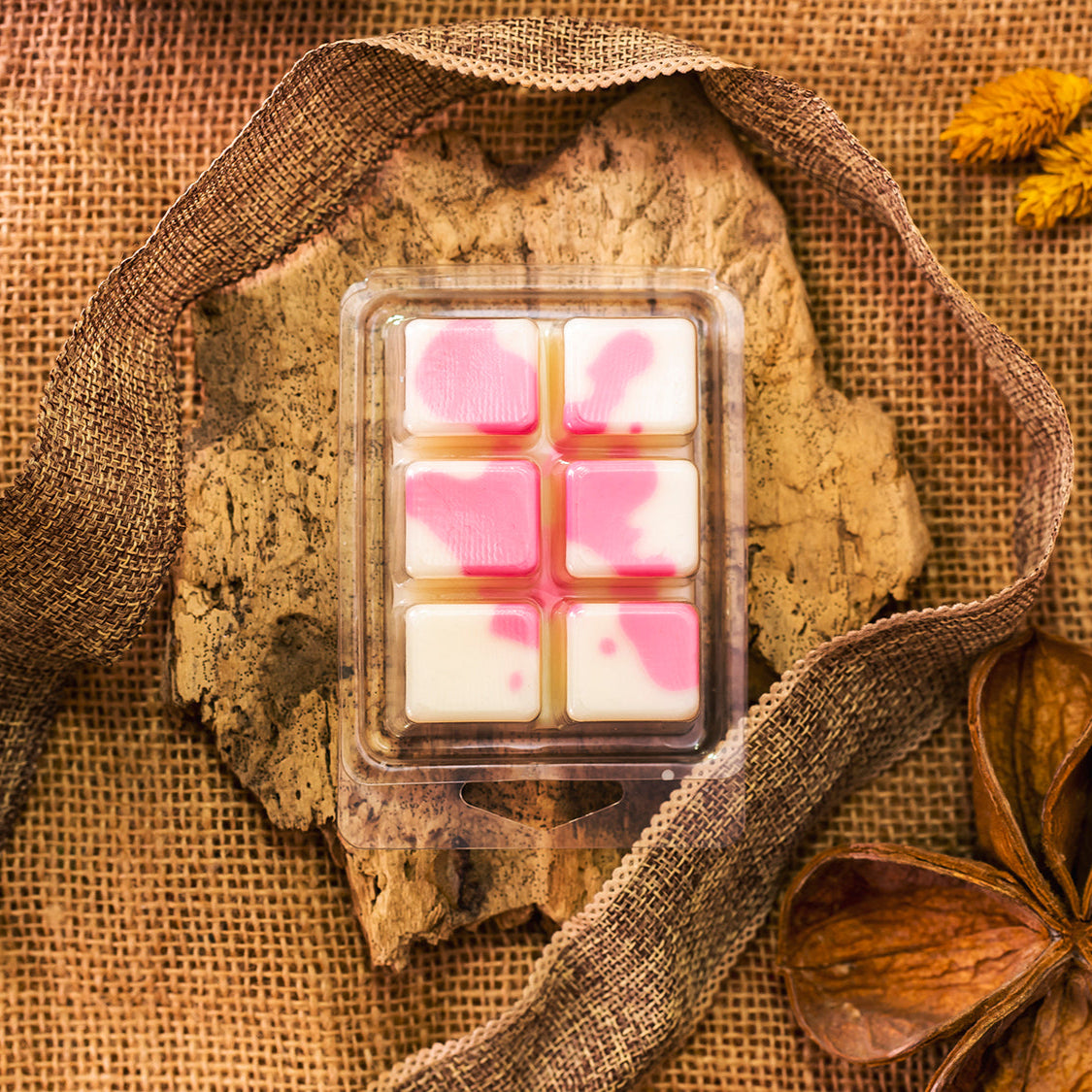 Un paquete de Wax Melts contiene seis trozos Barras de Chocolate DULZURA DE SANDÍA Fleur-de-Bois con remolinos rosas, colocadas sobre corteza y rodeadas de arpillera, cinta y flores secas para un regalo rústico personalizado.