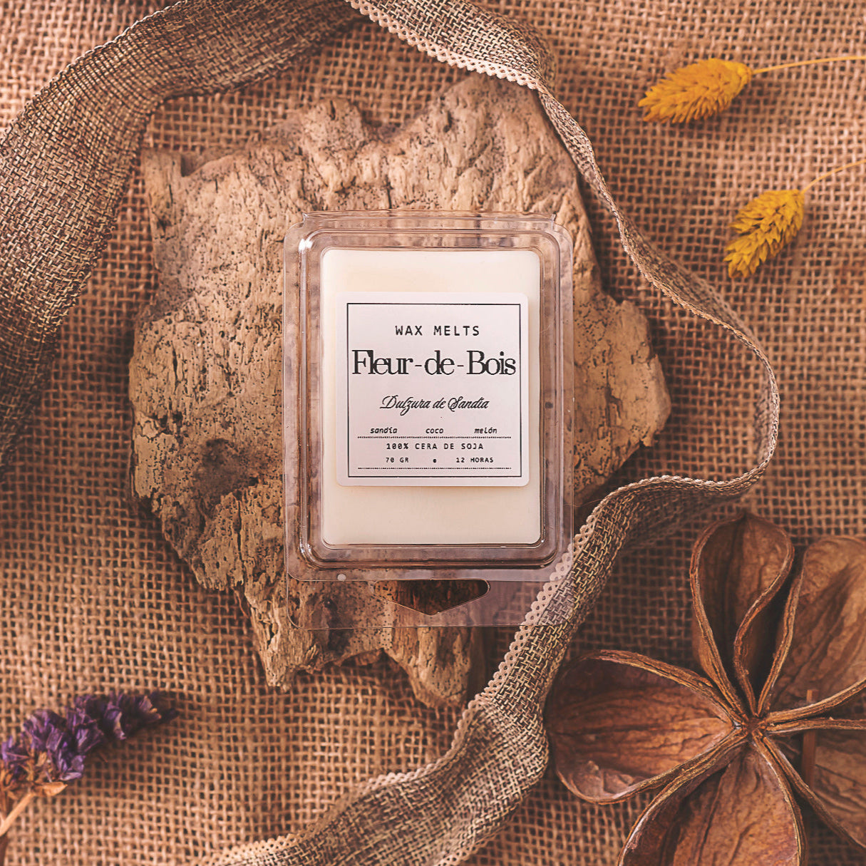 Un Wax Melts barra de chocolate DULZURA DE SANDÍA Fleur-de-Bois descansa sobre una corteza con arpillera, flores secas, cinta y una gran vaina de semillas para dar un toque rústico, ideal como regalo personalizado.