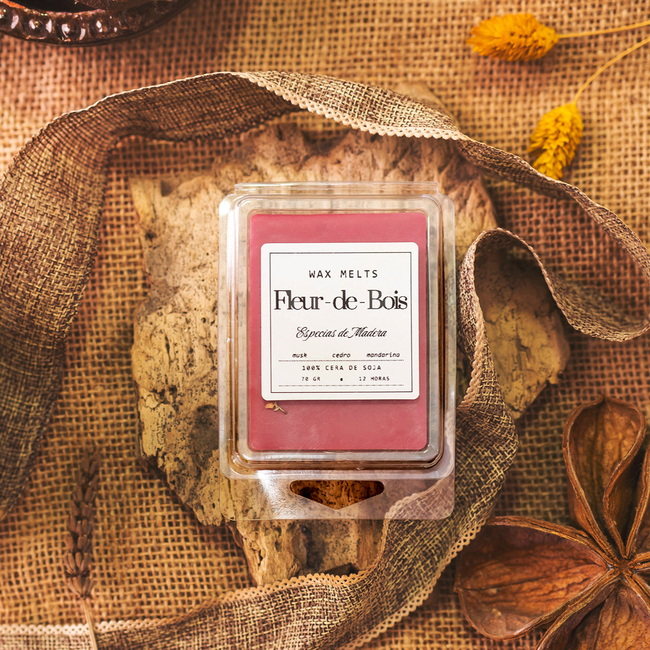 Un wax melts en Barra de Chocolate Fleur-de-Bois ESPECIAS DE MADERA de Fleur-de-Bois descansa sobre arpillera rústica, acentuada con flores secas y madera, evocando un acogedor ambiente artesanal y una cálida fragancia especias de madera.