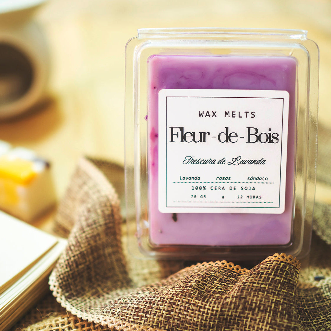 Primer plano de un paquete de Fleur-de-Bois Wax Melts Barra de chocolate FRESCURA DE LAVANDA, hechos a mano con cera de soja, con aromas de lavanda, rosa y sándalo, sobre arpillera y fondo desenfocado.