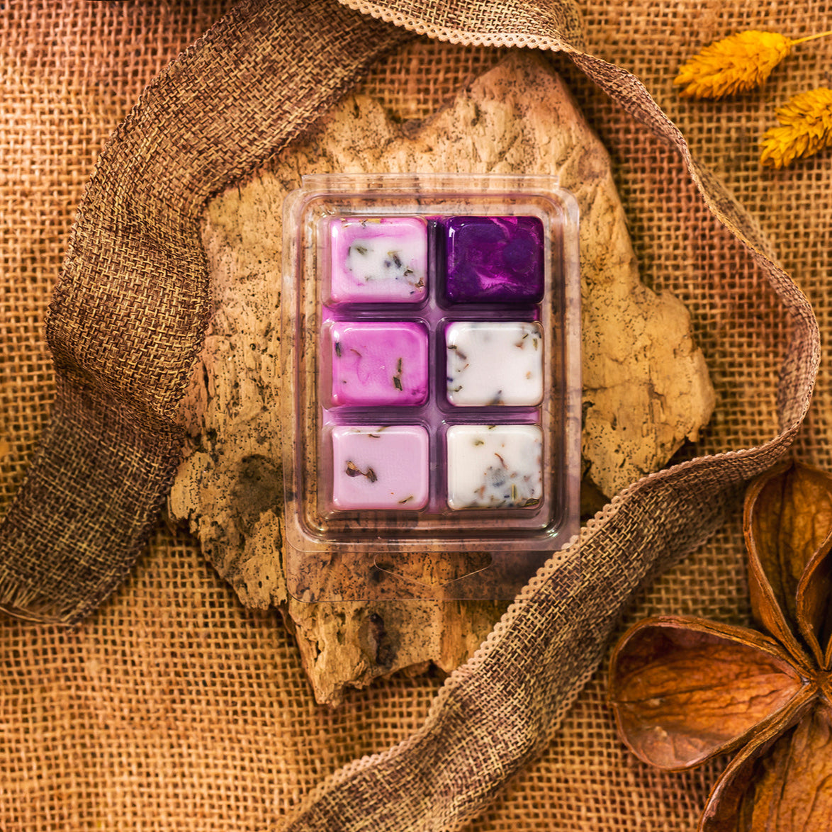 Un wax melt en forma de barra de chocolate rcon seis trozos Fleur-de-Bois púrpura y blanca Barra de chocolate FRESCURA DE LAVANDA hechos a mano con hierbas secas, expuestos sobre corteza con arpillera, flores secas y cinta para un aroma personalizado.