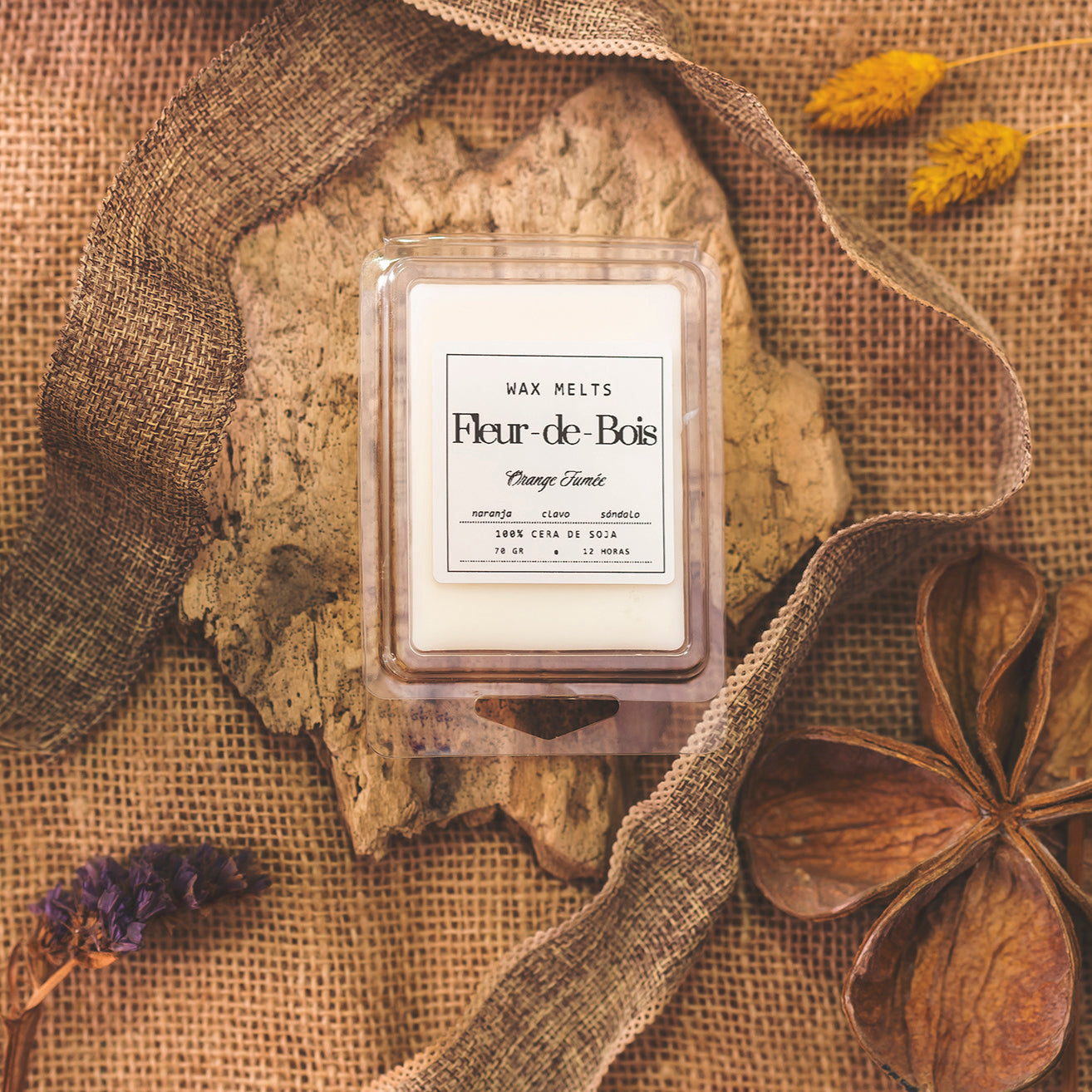 Un paquete de wax melts Fleur-de-Bois Wax Melts Barra de chocolate ORANGE FUMÉE descansa sobre madera rústica con arpillera, flores secas y un acento de madera, creando un ambiente acogedor, ideal como regalo personalizado.