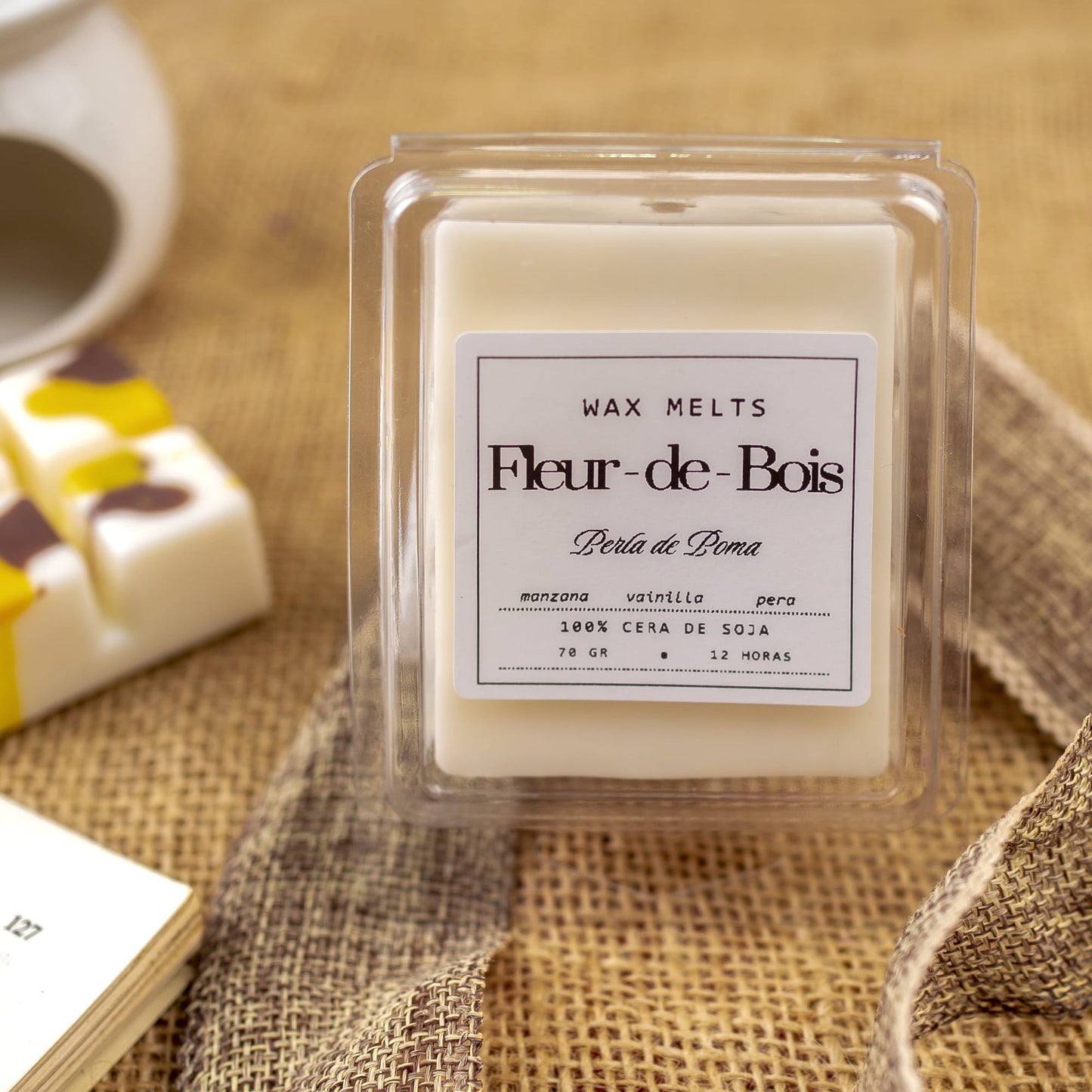 La Barra de chocolate fundido Fleur-de-Bois PERLA DE POMA de Fleur-de-Bois contiene cera de soja blanca con notas de manzana, vainilla y pera, ideal como regalo aromático. Se presenta en un envase transparente sobre arpillera.