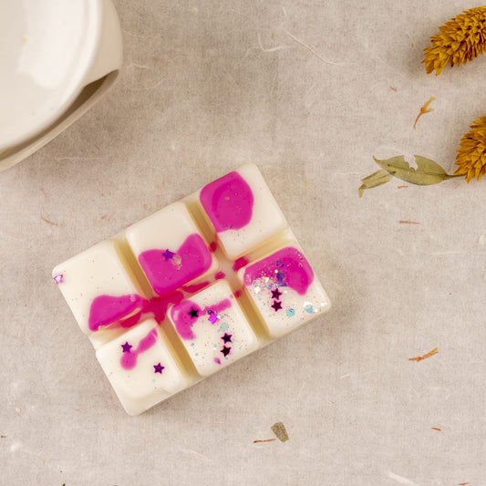 Wax Melts blancos y rosas jaspeados Barra de chocolate Fleur-de-Bois PERLA DE POMA de Fleur-de-Bois se disponen sobre una superficie texturizada con flores amarillas secas, hojas y un objeto redondo de cerámica-un regalo aromático perfecto.