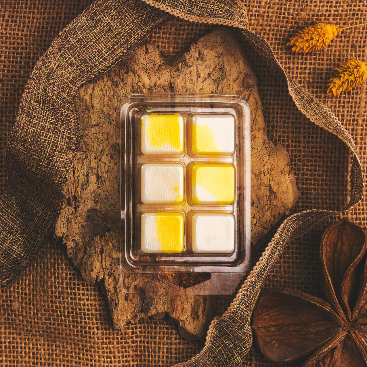 El wax melts Barra de chocolate de Cera de soja Fleur-de-Bois de PIE DE LIMÓN, con seis fundidos de cera cuadrados amarillos y blancos hechos a mano, se presenta sobre una superficie de madera rústica con arpillera, flores secas y decoración natural.