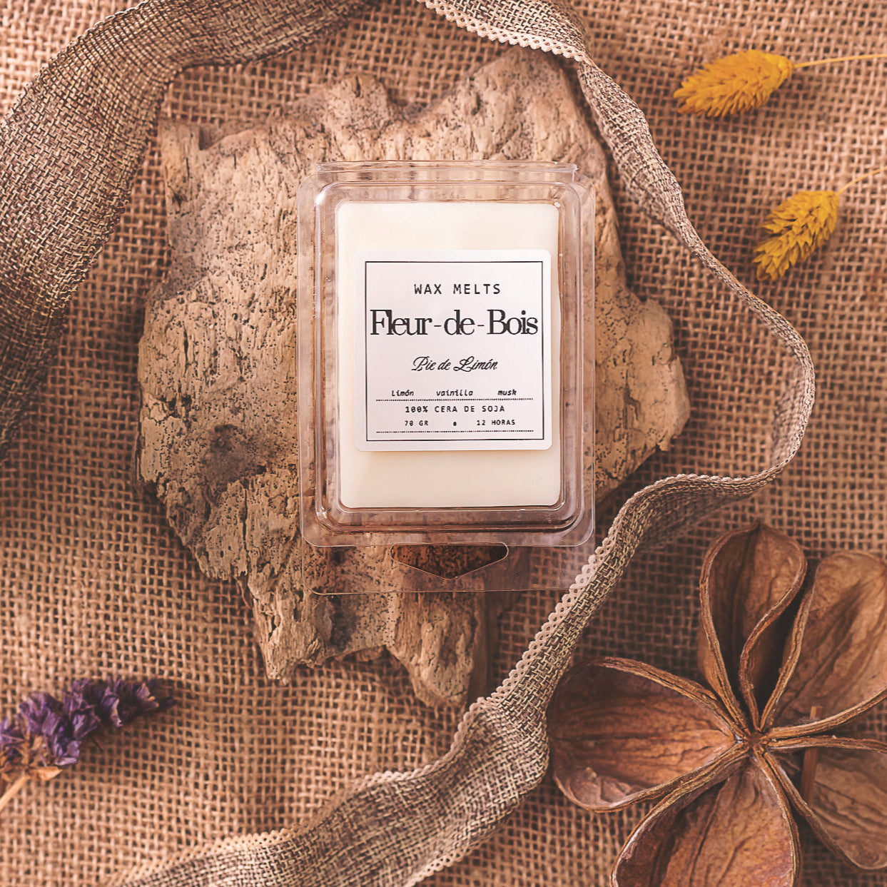 Un paquete de Wax Melts Barra de chocolate Fleur-de-Bois PIE DE LIMÓN de Fleur-de-Bois descansa sobre un trozo de corteza, acentuado con arpillera, flores secas y decoración natural terrosa.
