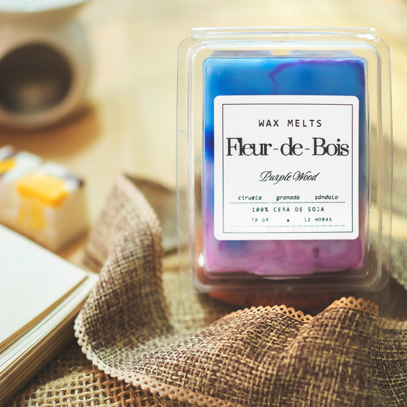 Un Wax Melts en forma de barra de chocolate PURPLE WOOD de Fleur-de-Bois, elaborada con cera de soja y perfumada con ciruela, granada y sándalo, descansa sobre arpillera, ideal como regalo personalizado.