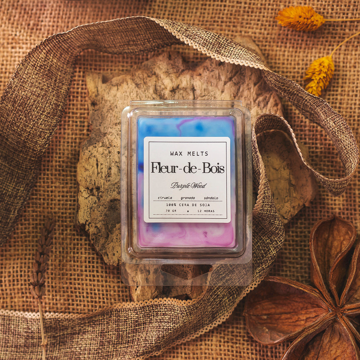 Una Barra de Chocolate Fleur-de-Bois Wax Melts Fleur-de-Bois PURPLE WOOD se asienta sobre arpillera con flores secas y cinta marrón. Los fundidos de cera de soja rosa, azul y morado forman un encantador regalo personalizado.