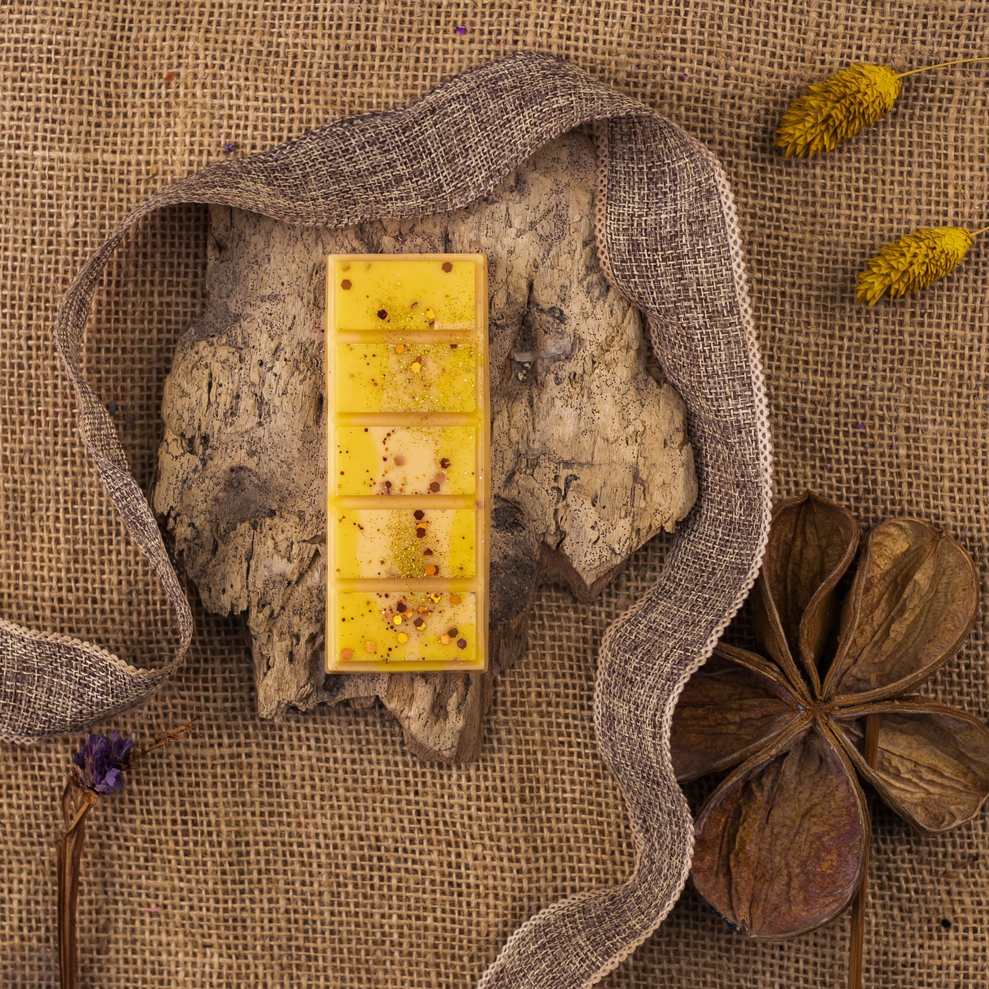 La cera amarilla Láminas Aromáticas Fleur-de-Bois PEAKY SPOOKY de Fleur-de-Bois se encuentra sobre una corteza entre cintas rústicas, flores secas y arpillera, evocando la calidez de las fragancias artesanales.
