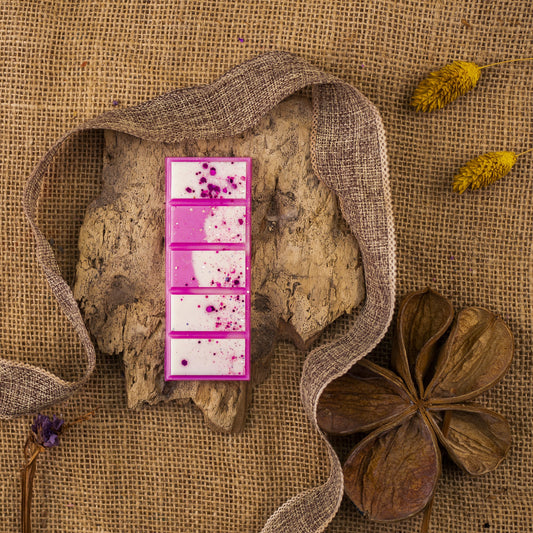 La Cera Fundida Láminas Aromáticas Fleur-de-Bois PERLA DE POMA de Fleur-de-Bois presenta motas blancas y rosas, desplegadas sobre corteza con flores secas y cinta, evocando fragancias elegantes.