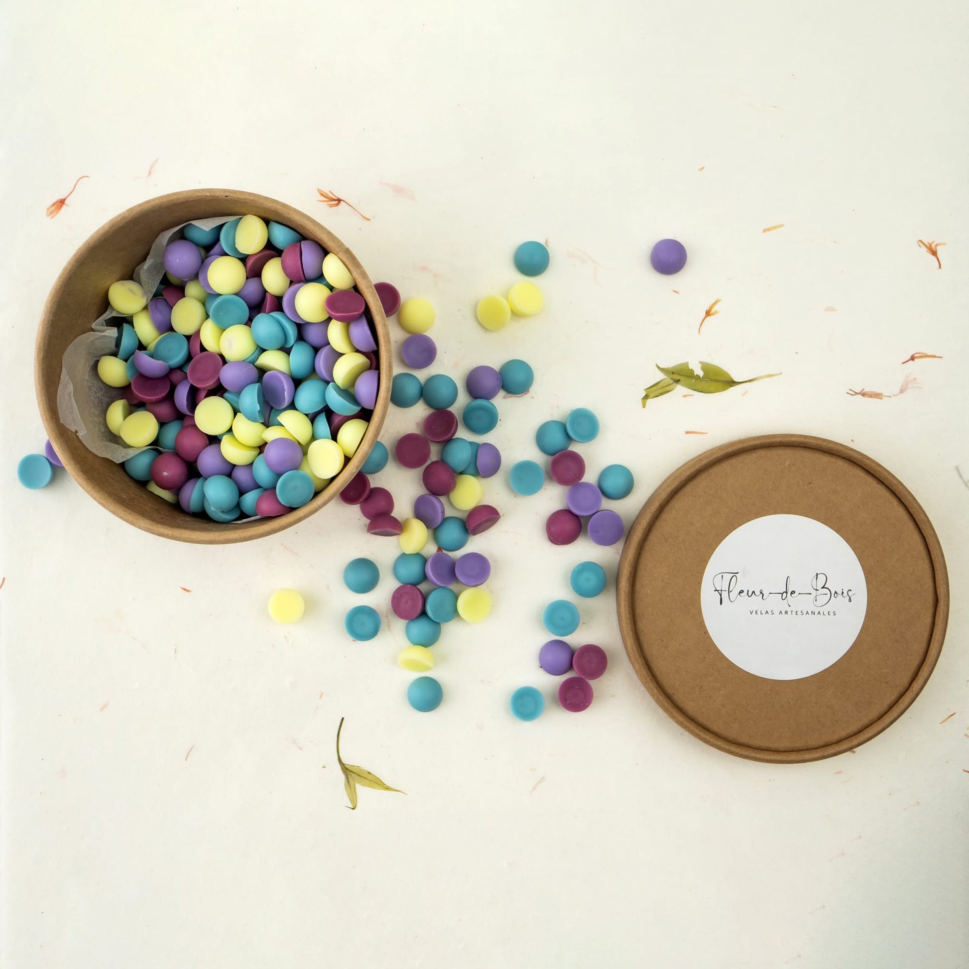 Una caja redonda de Fleur-de-Bois llena de coloridos Wax Melts Esencias en Miniatura CHISPITAS DE COLORES -morado, amarillo y verde azulado- recuerda a las golosinas artesanales. La tapa muestra la marca. Ideal para los aficionados a los aromas artesanales.
