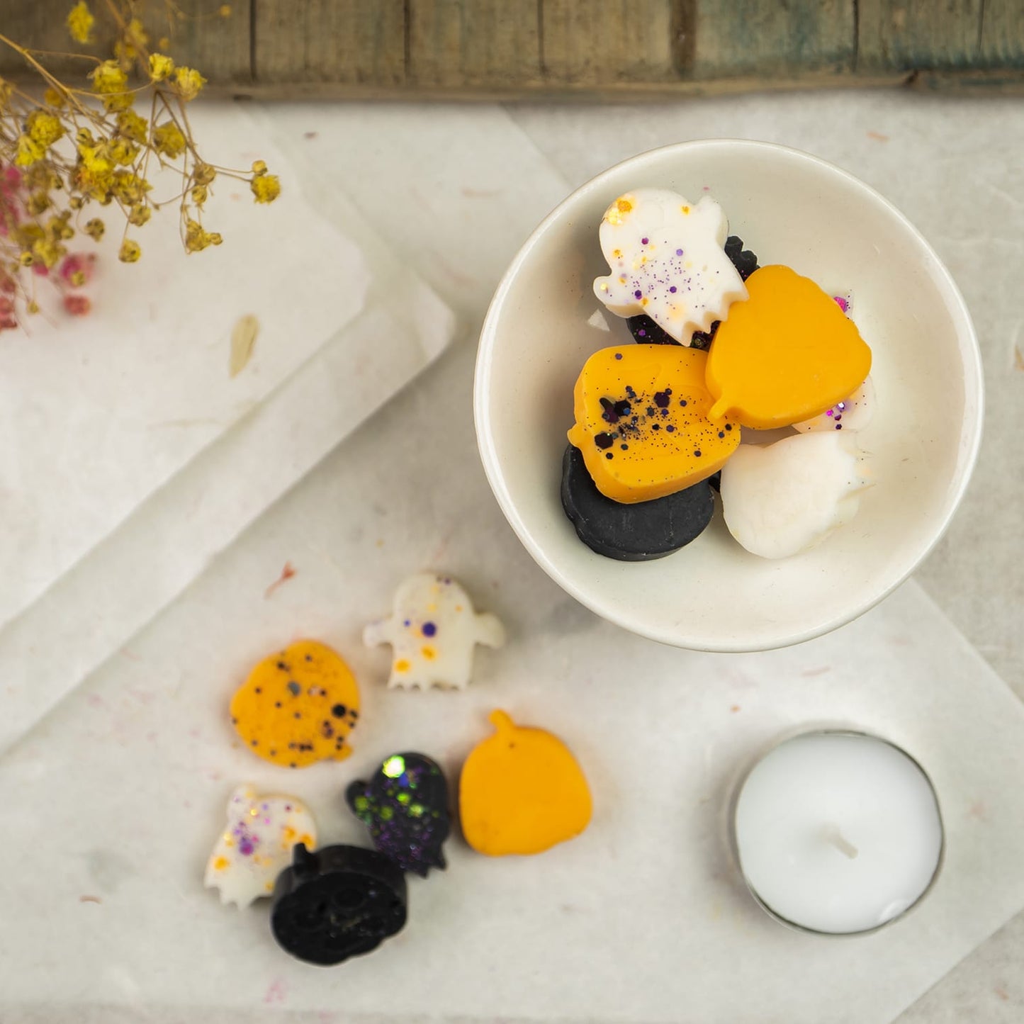 Un quemador con wax melts de Halloween en forma de fantasmas y calabazas se sienta en una mesa junto a más aperitivos, una candelita, flores secas, y Fleur-de-Bois Wax Melts Esencias en Miniatura CREEPY BOO PEAKY SPOOKY fragancia calabaza.