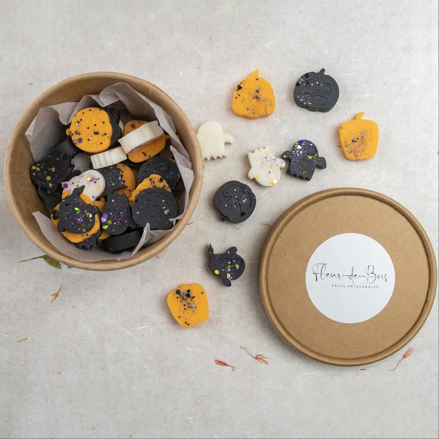 Una caja redonda llena de galletas de Halloween con forma de calabazas, fantasmas y murciélagos en colores negro, naranja y blanco con espolvoreado-evocando Fleur-de-Bois Wax Melts Esencias en Miniatura CREEPY BOO PEAKY SPOOKY. Varias galletas están esparcidas fuera de la caja.